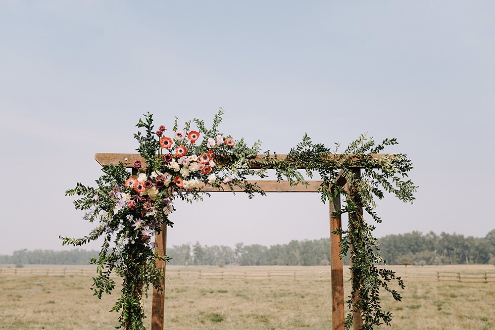 wooden arch in Montana pasture decorated with greenery and pink and mauve flowers
